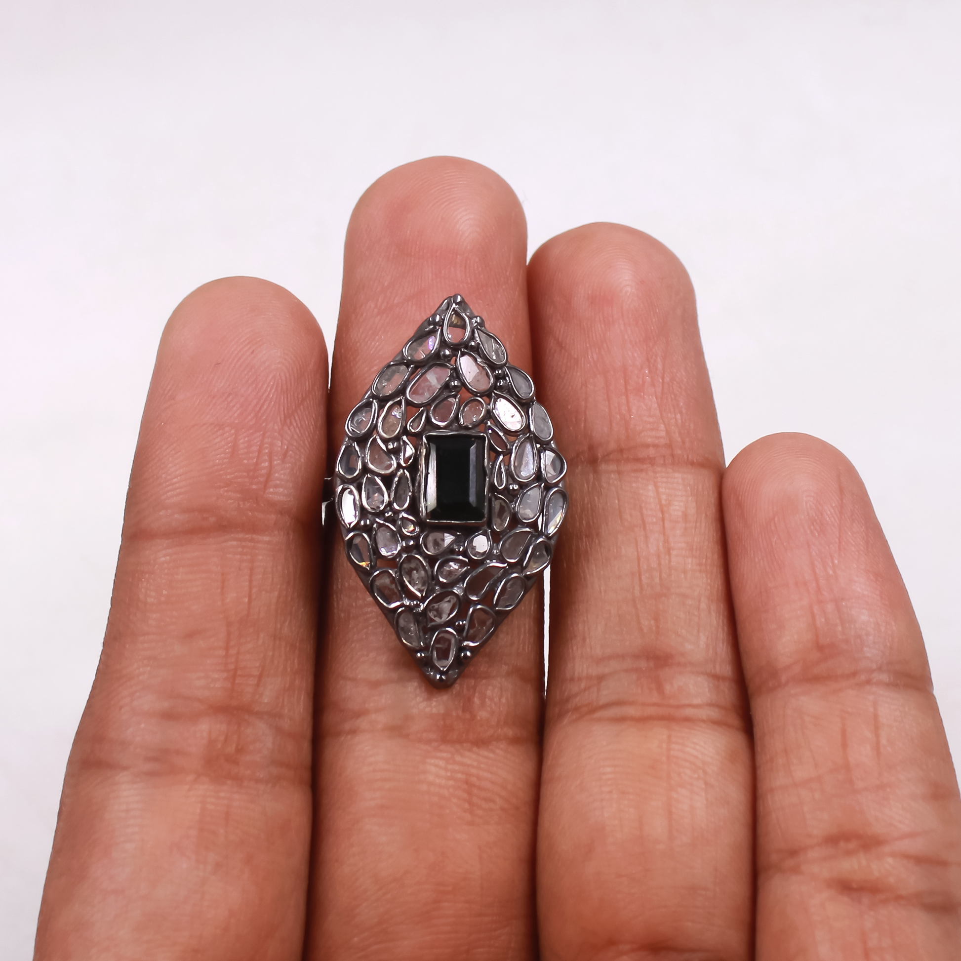 Silver ring with black gemstone held between fingers on a white background