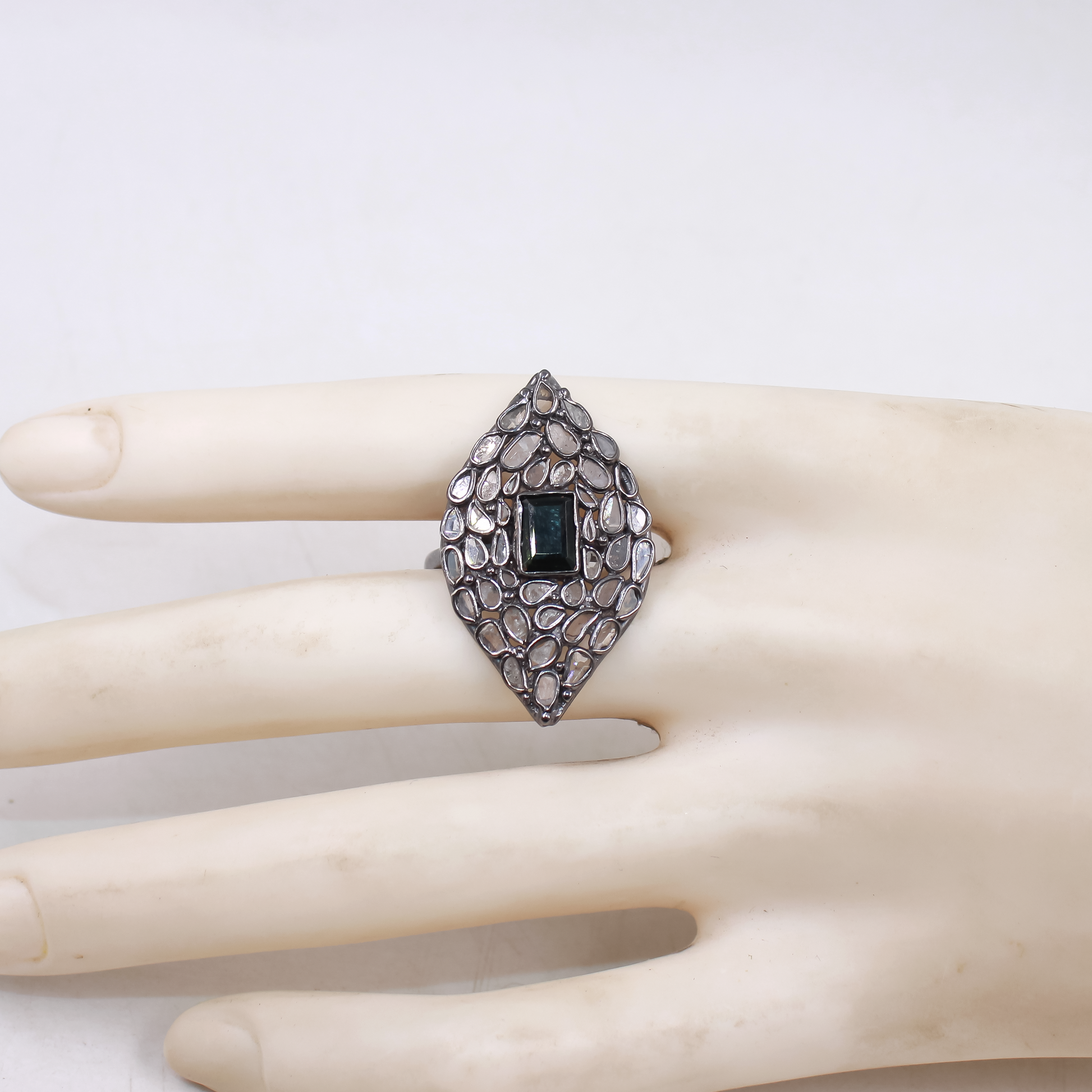 Silver ring with a central gemstone on a mannequin hand against a white background