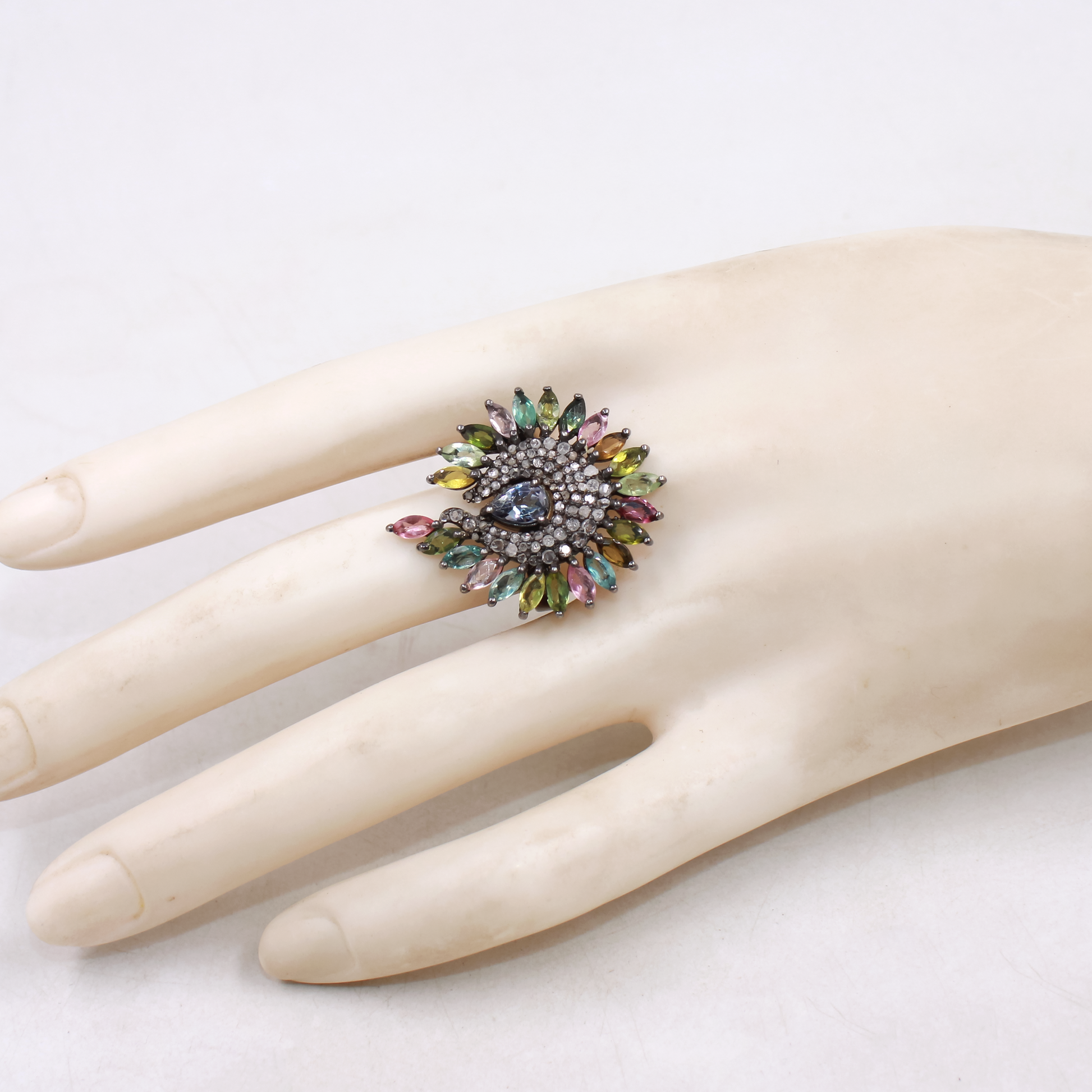 Multicolored gemstone ring on a mannequin hand against a white background