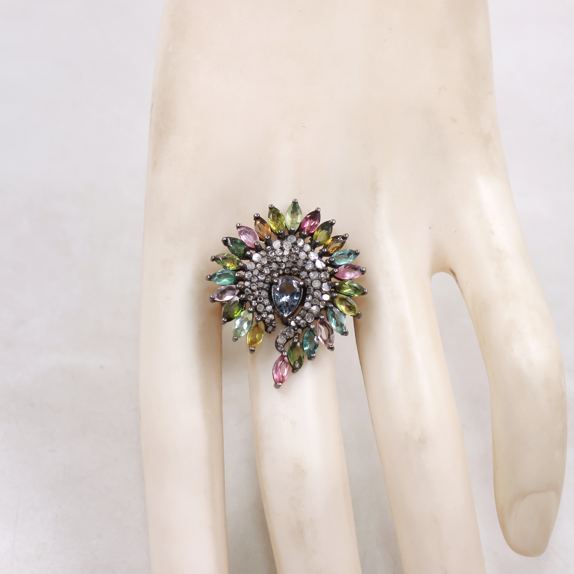 Multicolored gemstone ring on a mannequin hand against a white background