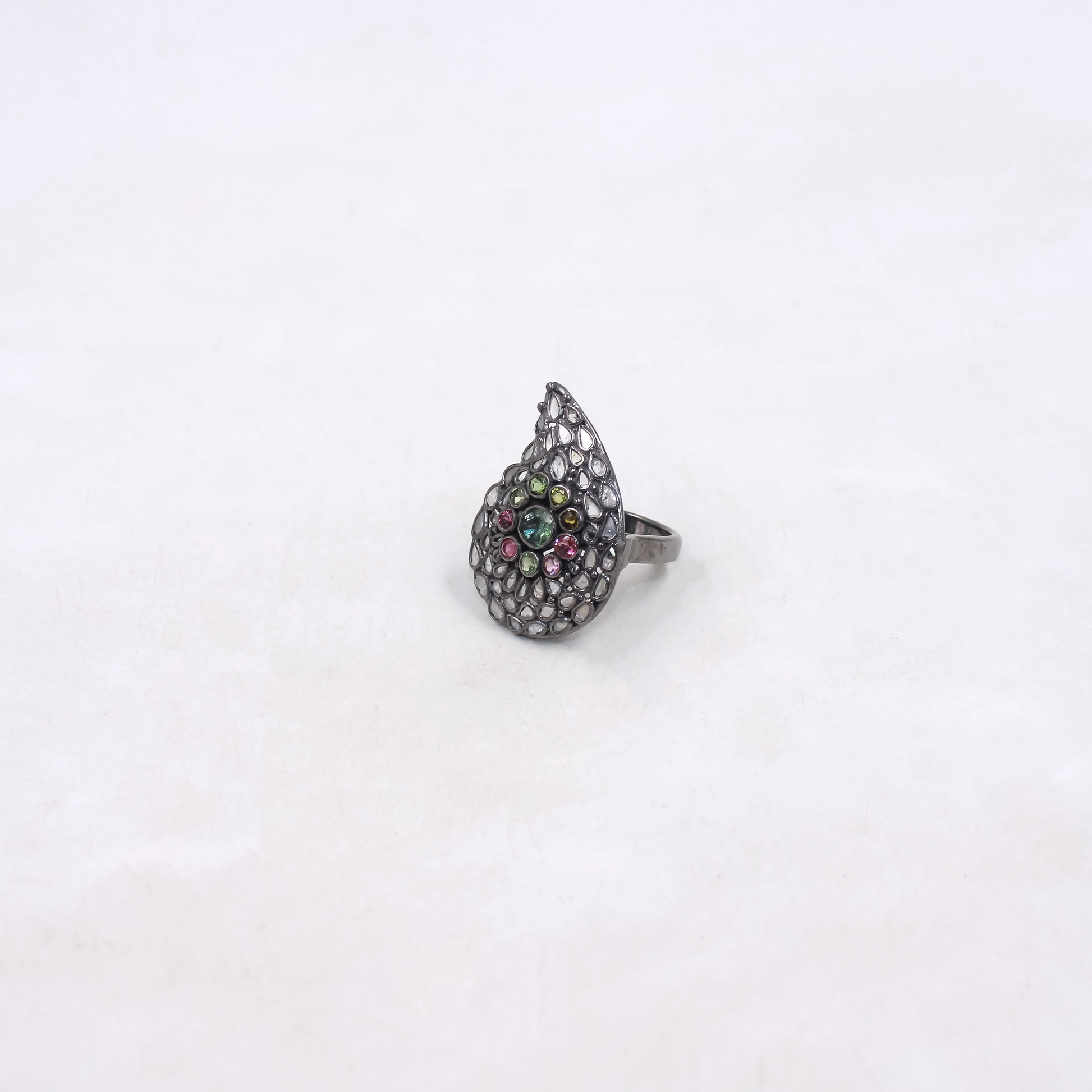 Teardrop-shaped ring with colorful gemstones on a white background