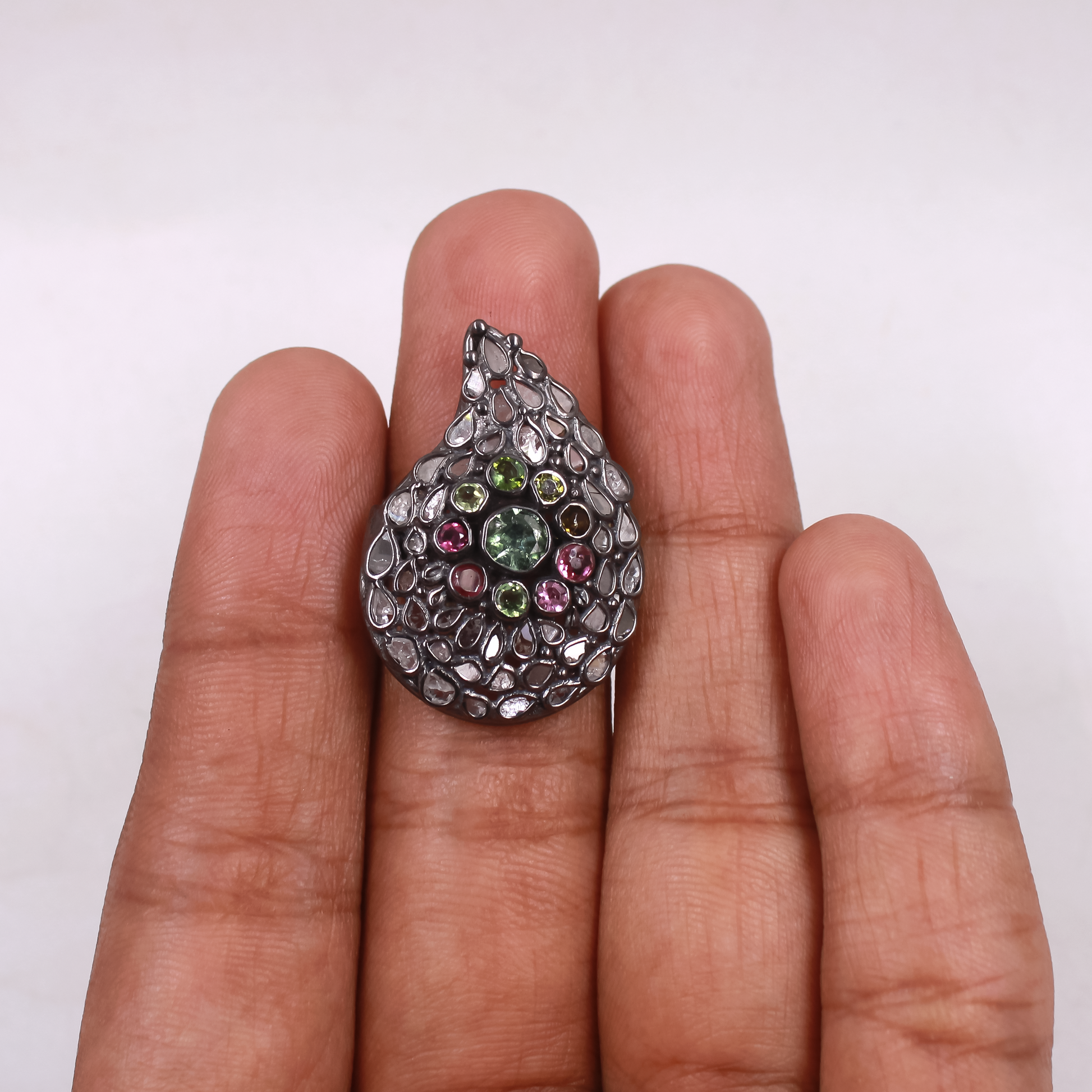 Teardrop-shaped gemstone ring held between fingers on a white background
