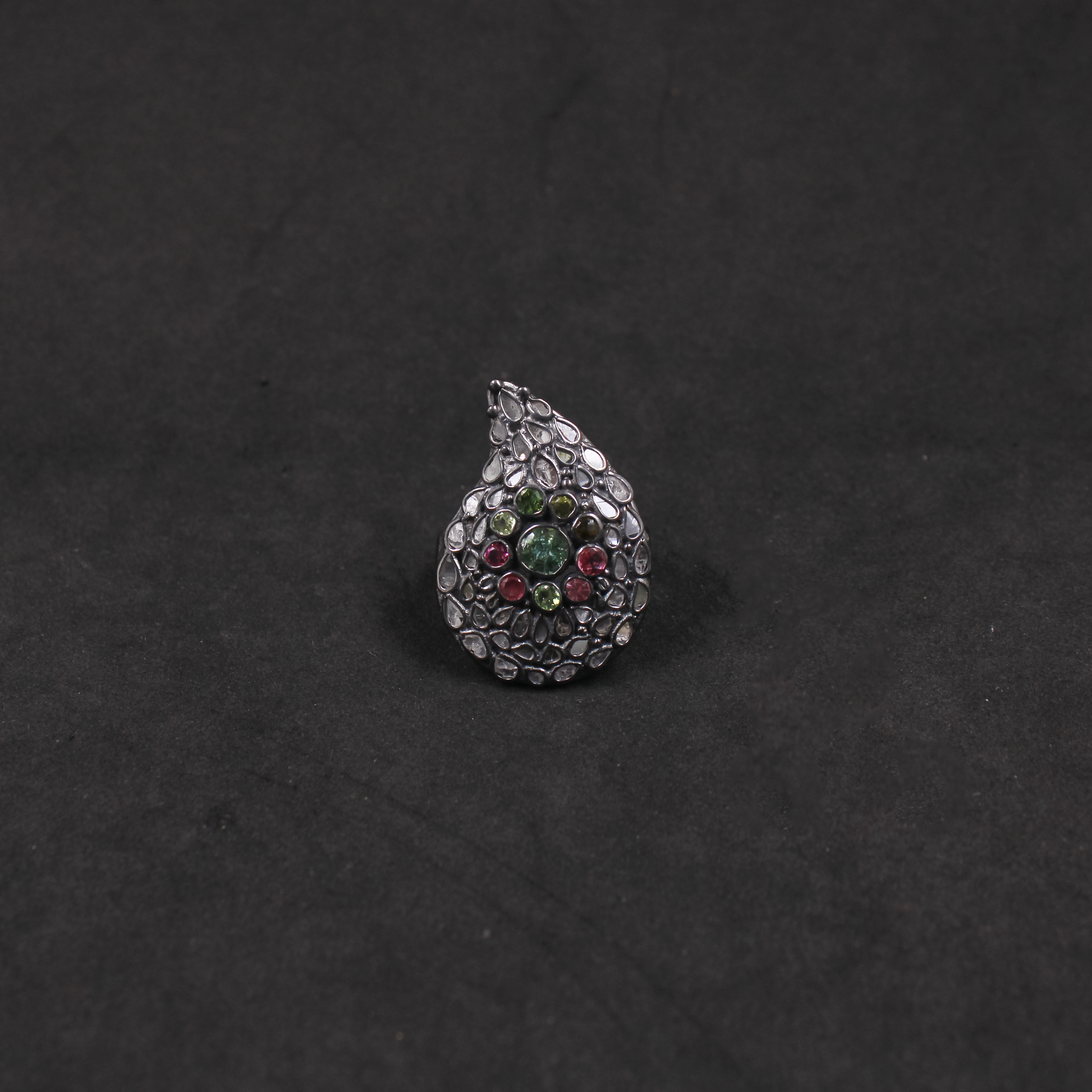 Teardrop-shaped silver ring with colored gemstones on a black background