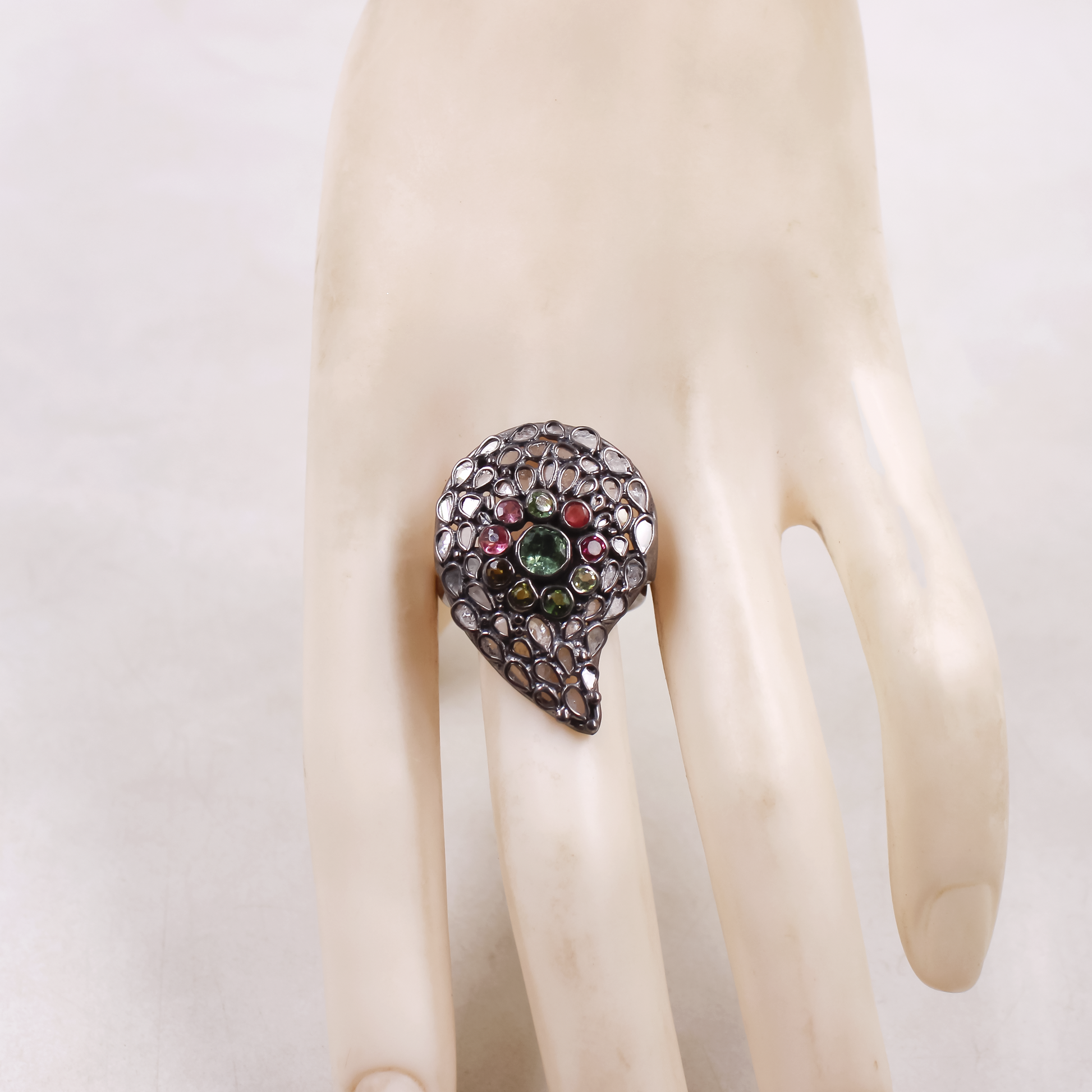 Teardrop-shaped ring with multicolored gemstones on a mannequin hand against a white background