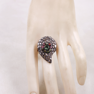 Teardrop-shaped ring with multicolored gemstones on a mannequin hand against a white background