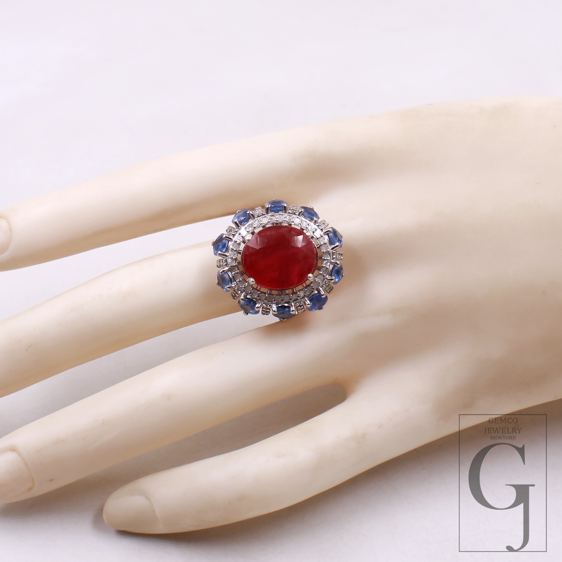 Ring with a red gemstone and blue accents on a mannequin hand, with a visible brand logo.