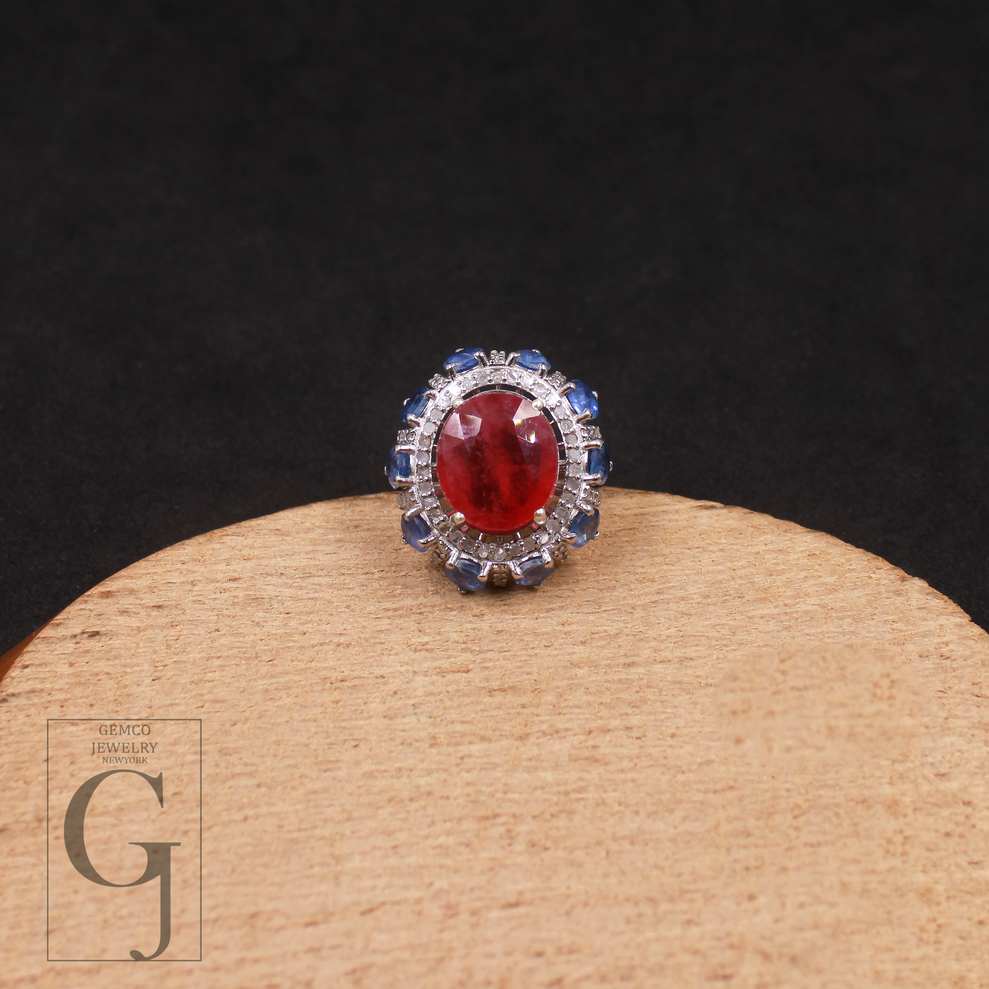 Ring with a red gemstone and blue accents on a wooden stand with a dark background