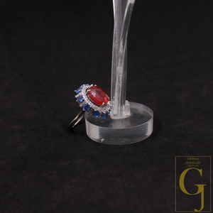 Ring with red gemstone and blue accents on a clear stand against a black background, featuring the Gemco Jewelry logo.