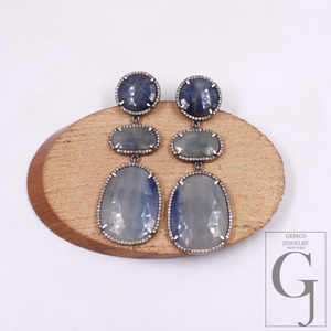 Pair of earrings with gemstones on a wooden stand, brand 'Gemco Jewelry' visible.