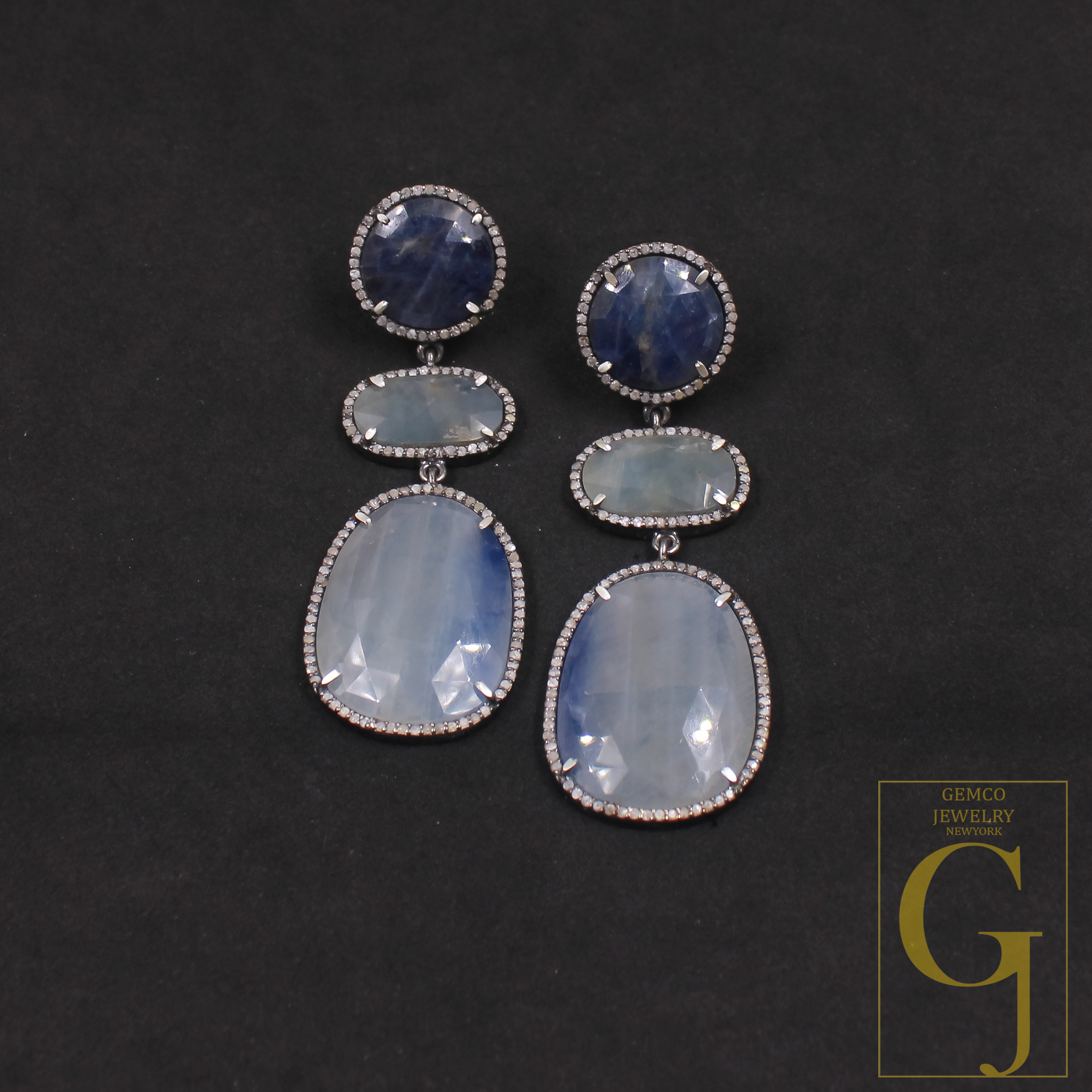 Pair of earrings with Blue Sapphire on a dark background, featuring the Glimco Jewelry logo.