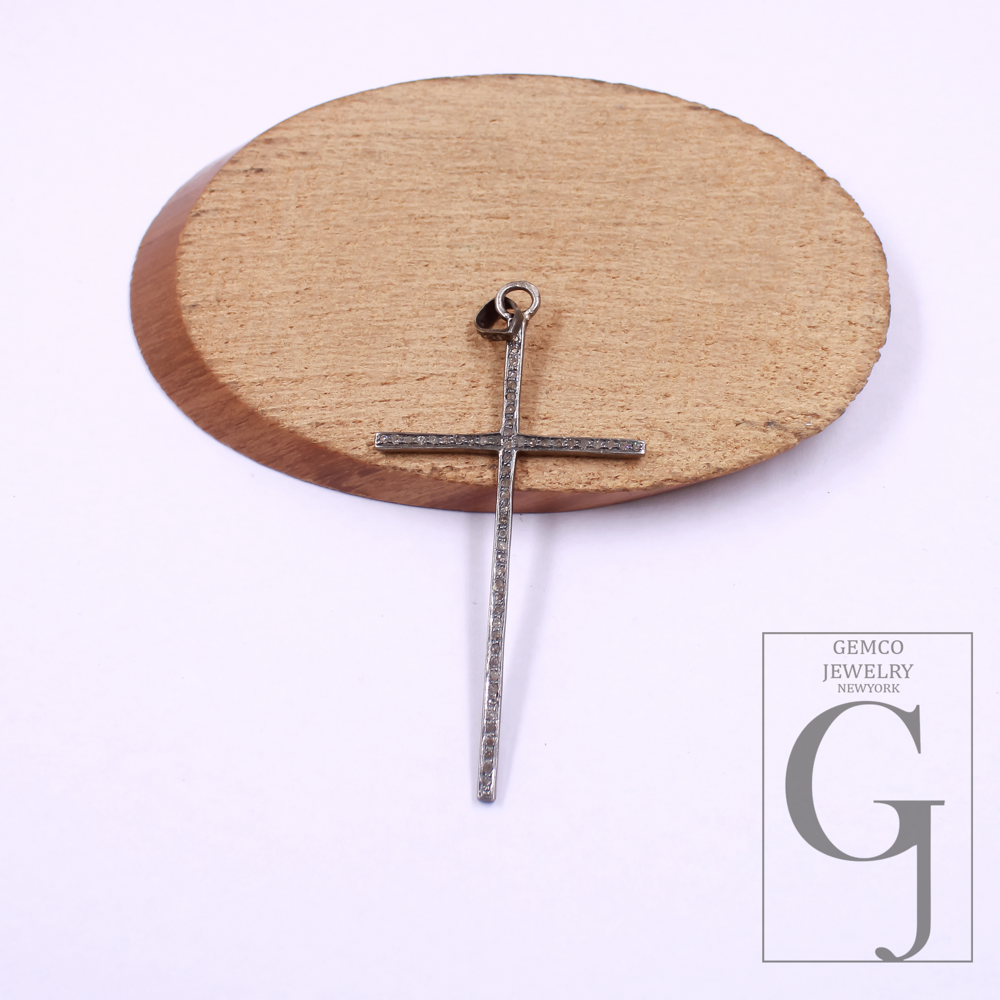 Silver cross pendant on a wooden stand with Gemco Jewelry.