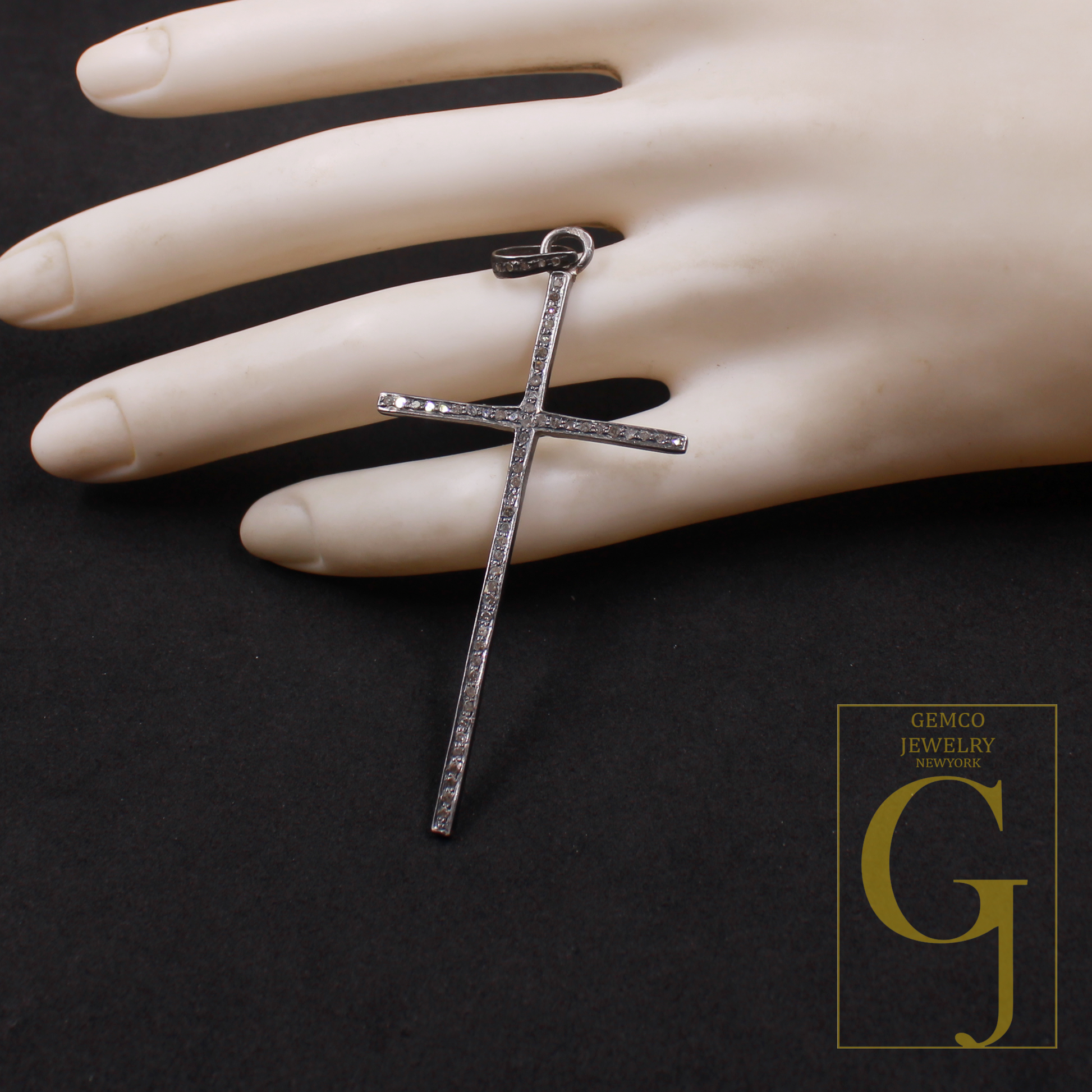 Silver cross pendant on a mannequin hand with Gemco Jewelry New York logo.