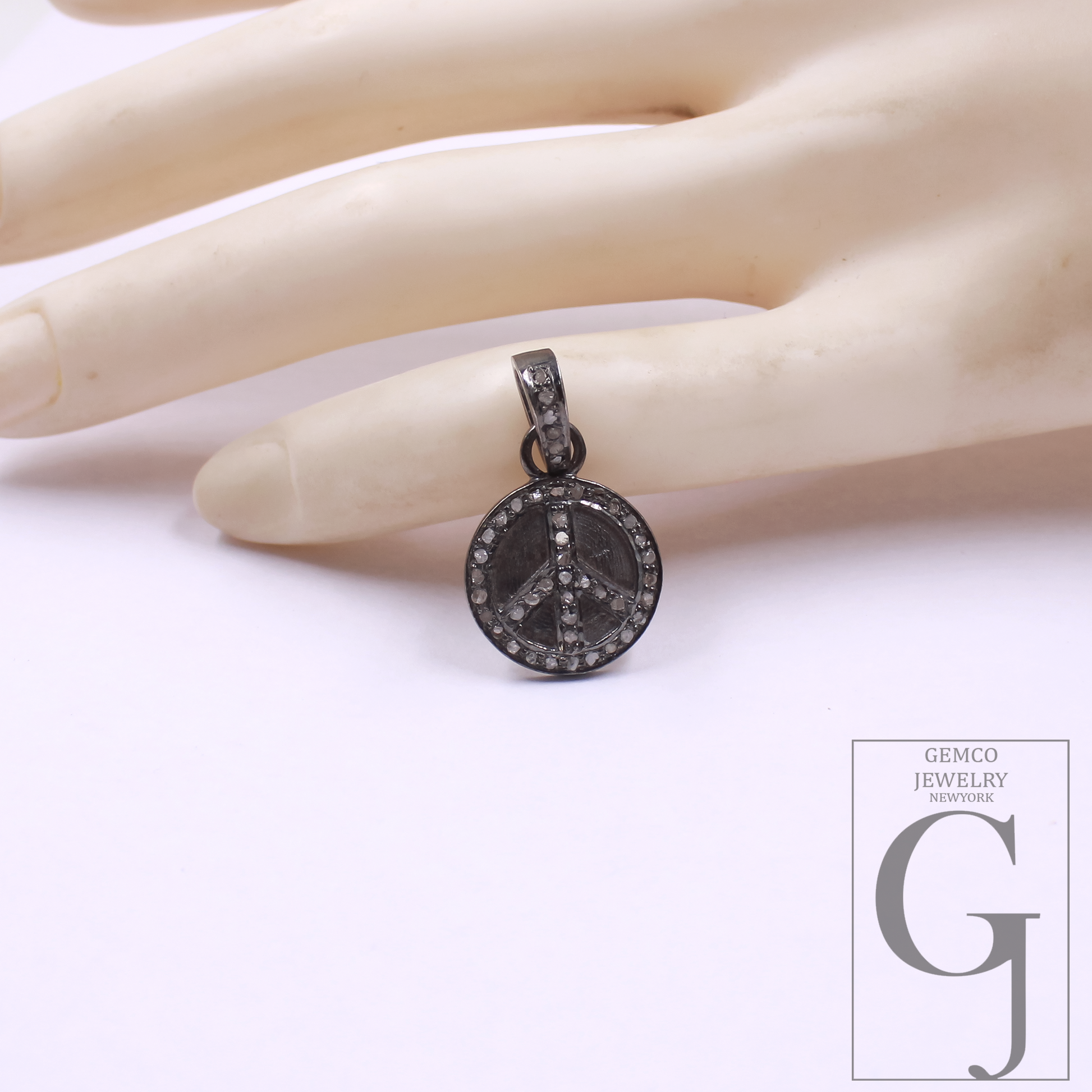 Peace symbol pendant on a hand with Gemco Jewelry logo in the corner