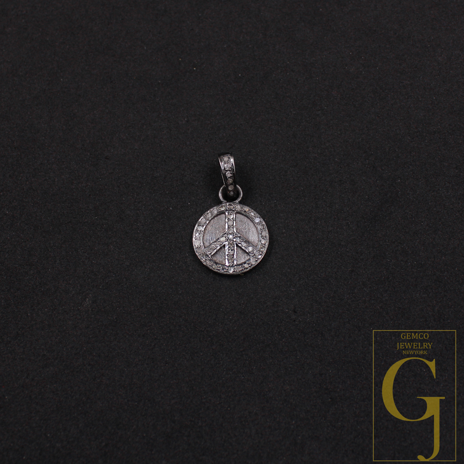 Silver peace symbol pendant on a black background with Gemco Jewelry logo.