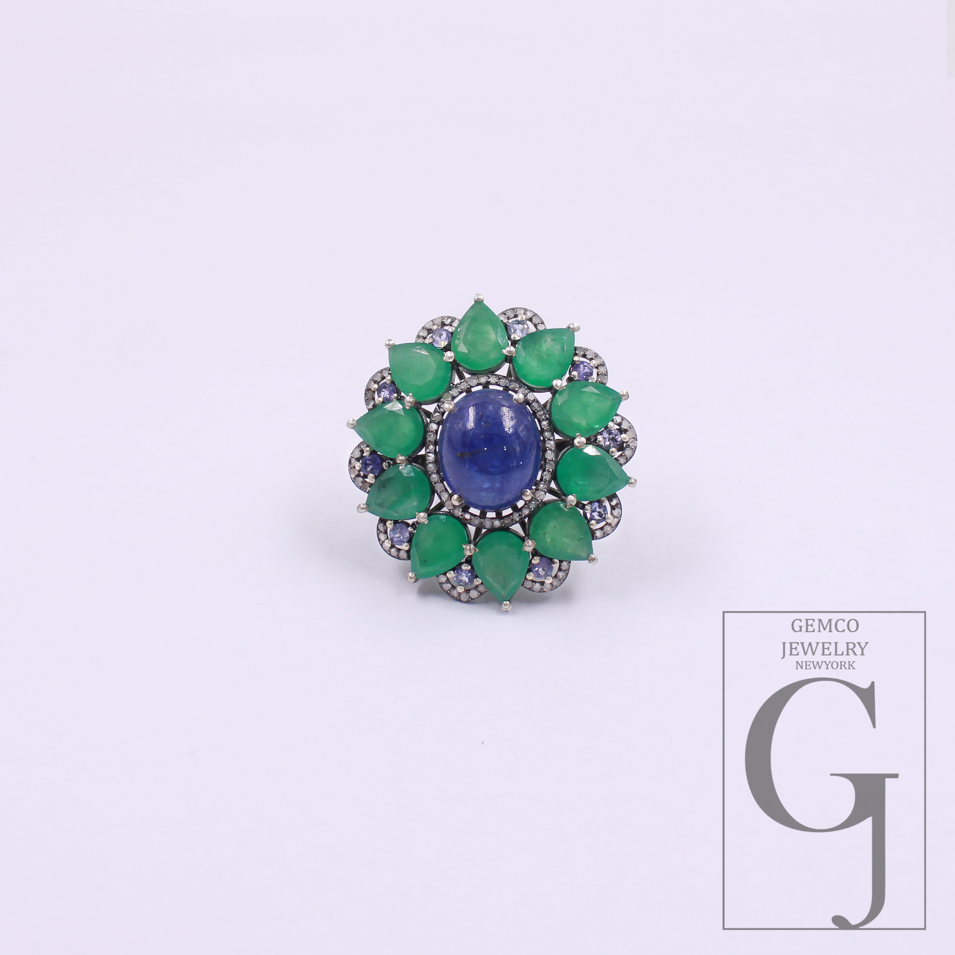 Jewelry ring with green gemstones and a blue center on a white background, featuring the Gemco Jewelry logo.