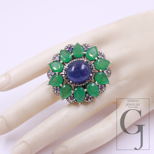 Ring with green gemstones and a blue center stone on a mannequin hand, with Gemco Jewelry branding.