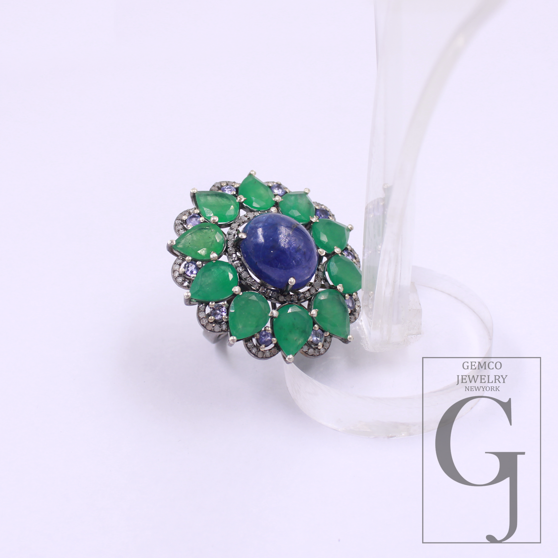 Ring with green gemstones and a blue central stone on a white background, featuring Gemco Jewelry branding.