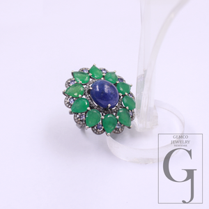 Ring with green gemstones and a blue central stone on a white background, featuring Gemco Jewelry branding.