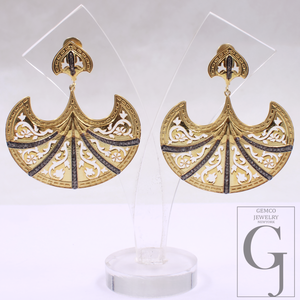 Gold earrings with intricate designs on a clear stand, branded 'Gemco Jewelry'.