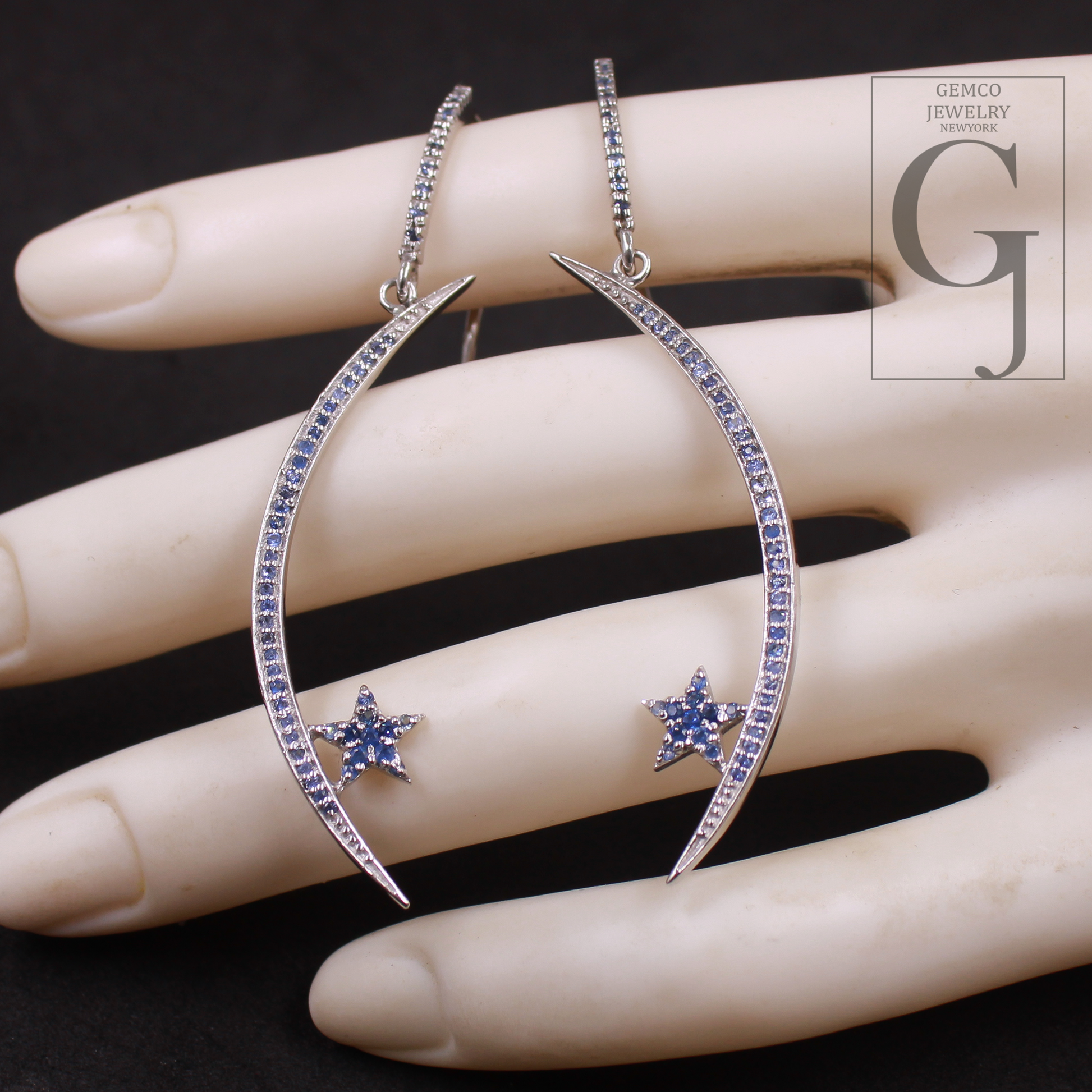 Crescent moon and star earrings on a hand with Gemco Jewelry logo.