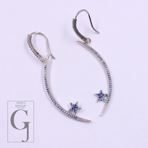 Pair of silver earrings with star and crescent moon designs on a light purple background, featuring Gemco Jewelry New York logo.