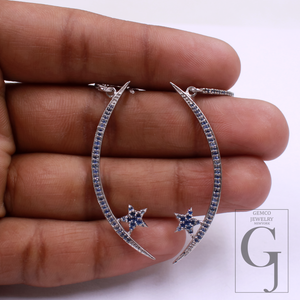 Silver hoop earrings with star details held between fingers on a white background, Gemco Jewelry brand visible.