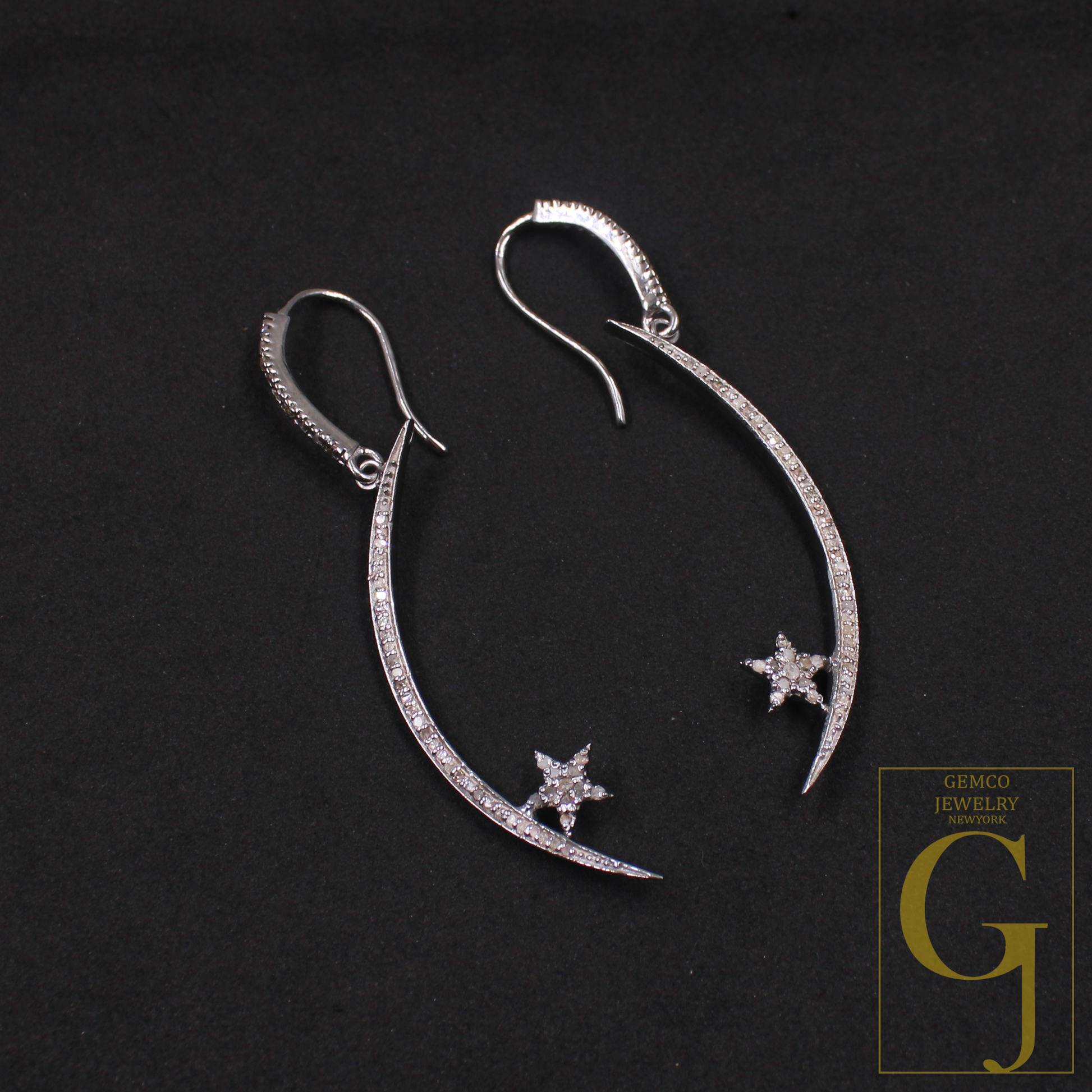 Silver earrings with star and crescent moon designs on a dark background, featuring Gemco Jewelry logo.