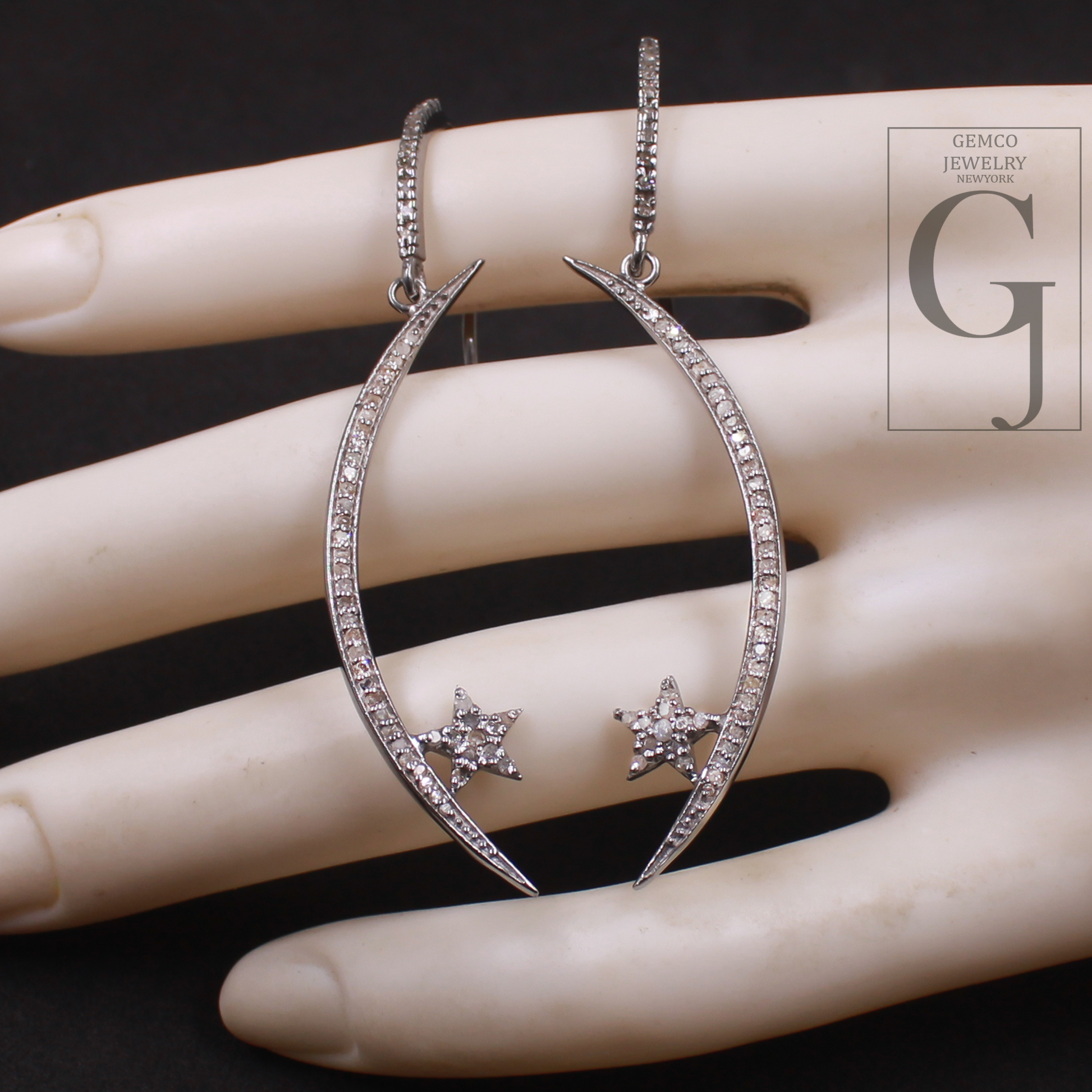 Silver hoop earrings with star details on a mannequin hand, featuring Gemco Jewelry logo.