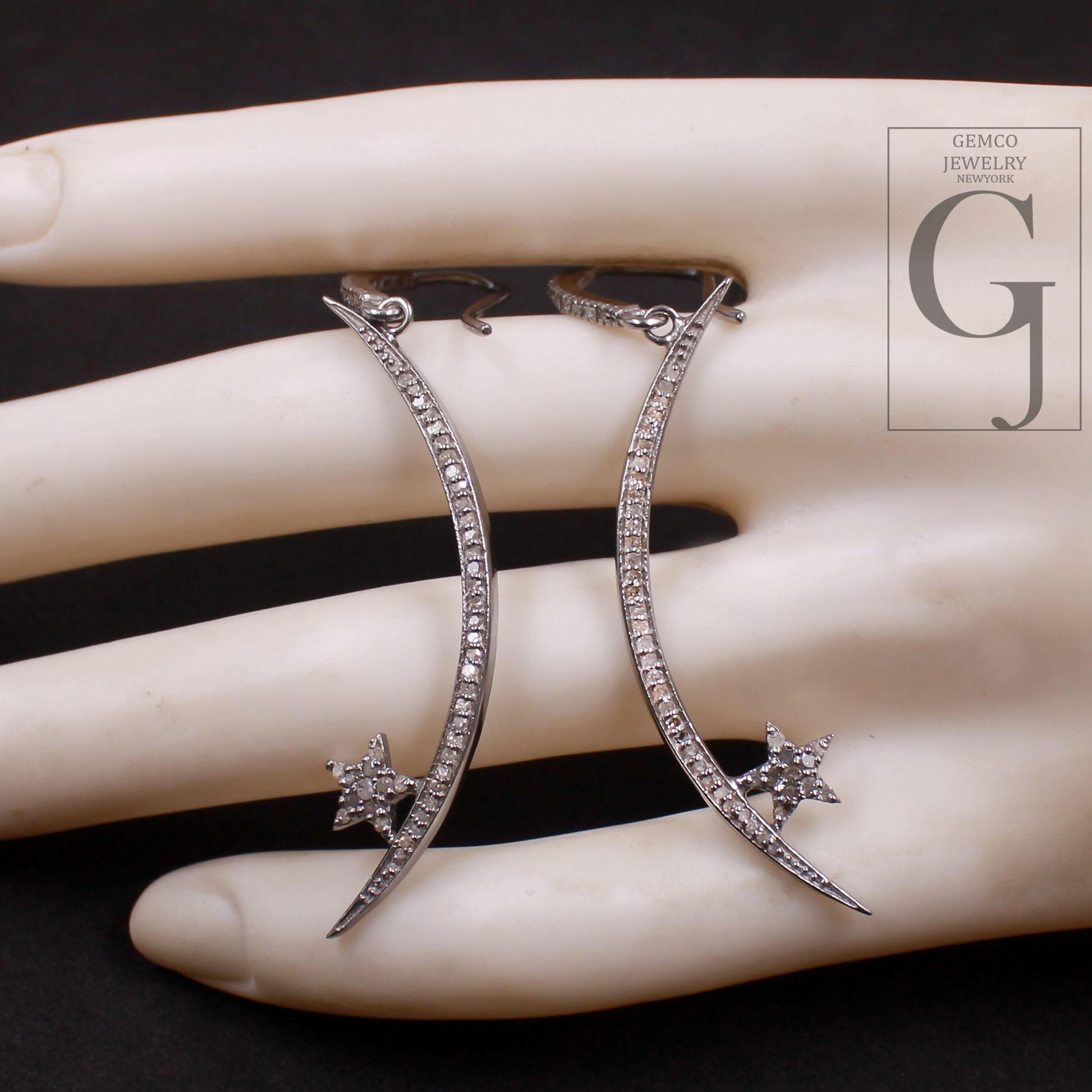 Silver earrings with star details on a hand, brand 'GEMCO JEWELRY' visible