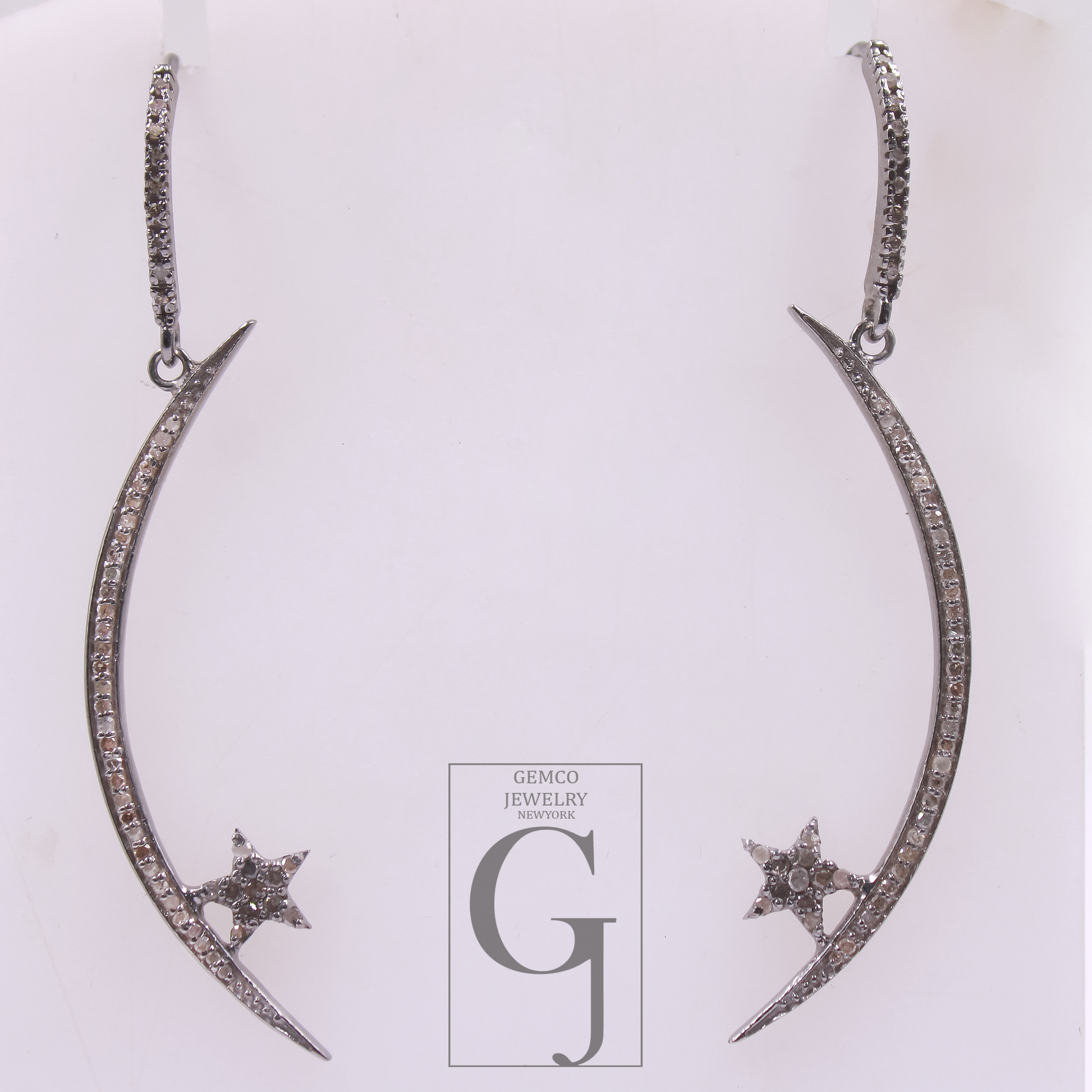 Pair of silver earrings with star designs on a white background, featuring the Gemco Jewelry logo.
