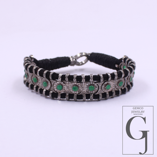 A silver-toned bracelet featuring black rectangular inlays and round green gemstone accents, displayed on a light lavender background with a Gemco Jewelry Shop logo in the bottom right corner.