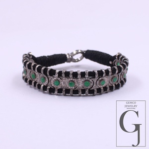 A silver-toned bracelet featuring black rectangular inlays and round green gemstone accents, displayed on a light lavender background with a Gemco Jewelry Shop logo in the bottom right corner.