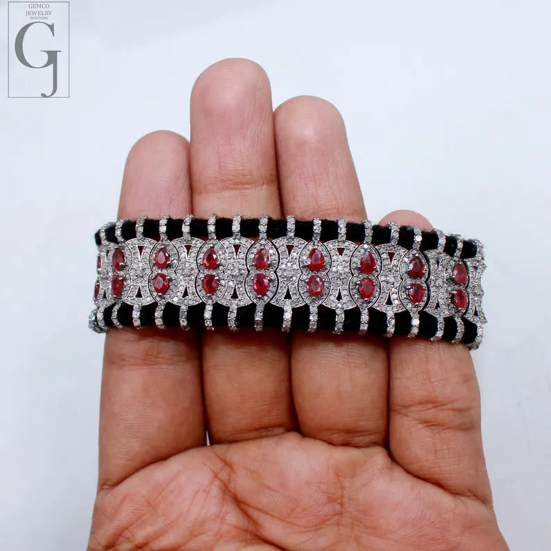 Jewelry bracelet with red stones and black accents held on a hand against a white background