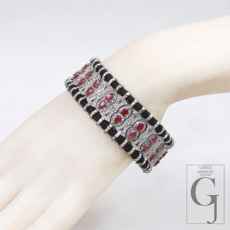 Black bracelet with red stones on a white arm against a light gray background, with 'GEMCO JEWELRY' branding.