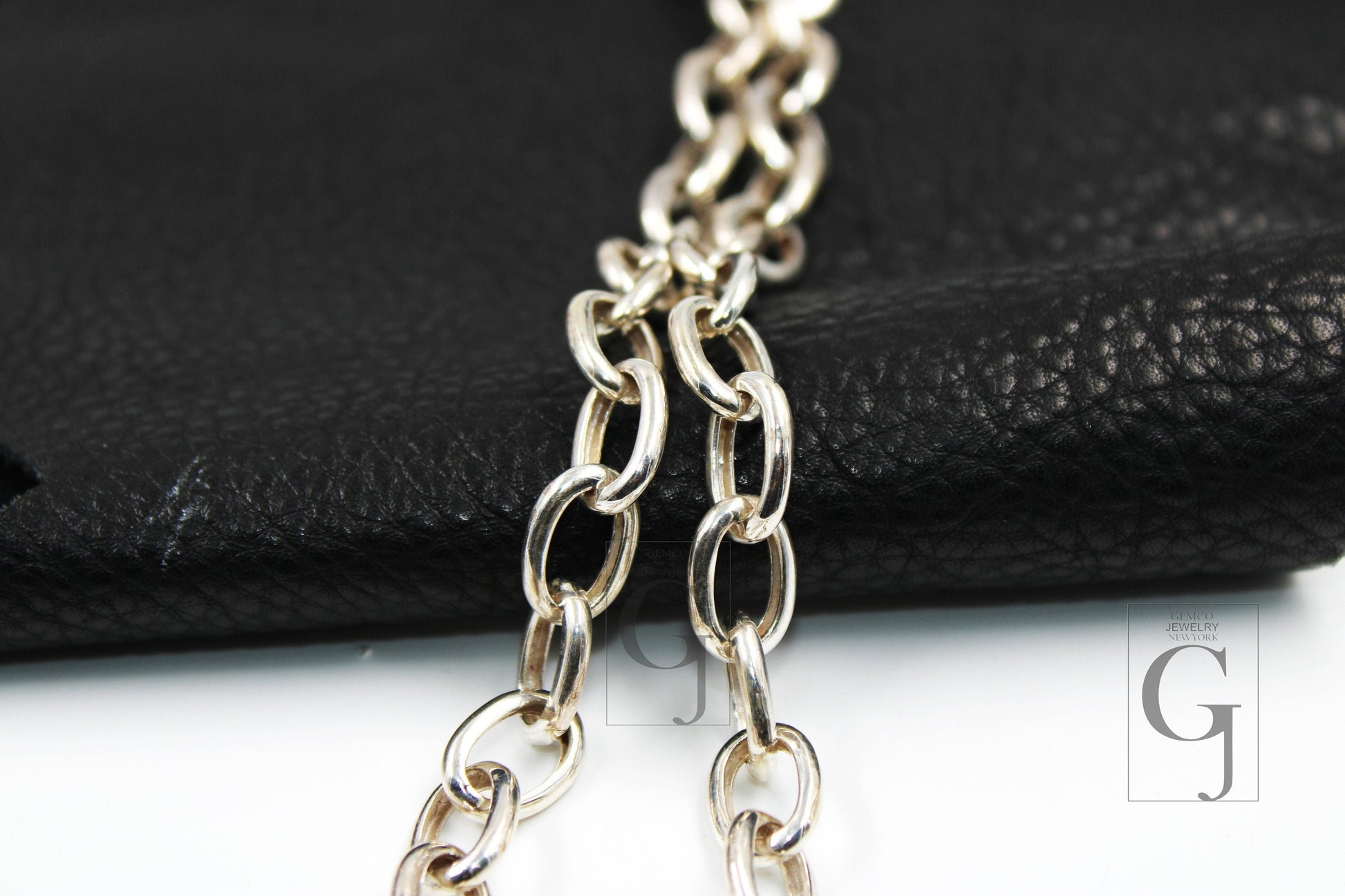 Close-up of a silver white link chain necklace laid out on a black surface.