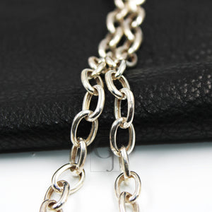Close-up of a silver white link chain necklace laid out on a black surface.